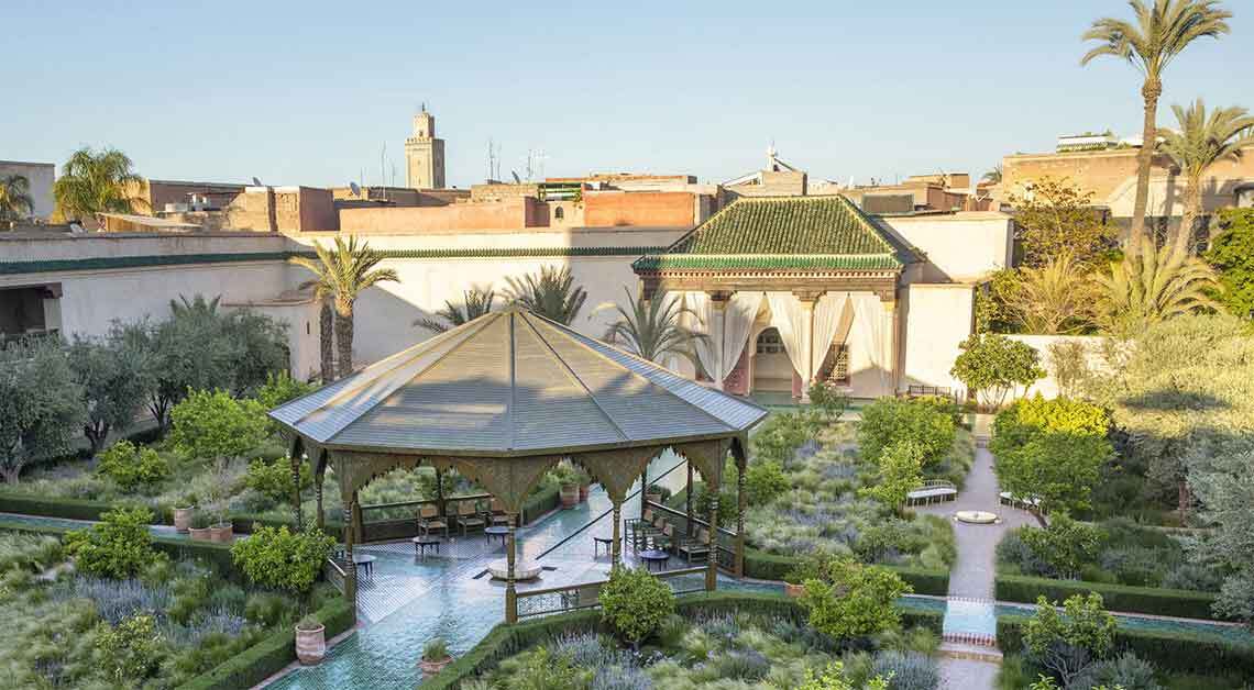 eco-Luxury Moroccan resort garden with lush greenery, a traditional pavilion, and elegant architecture in the background